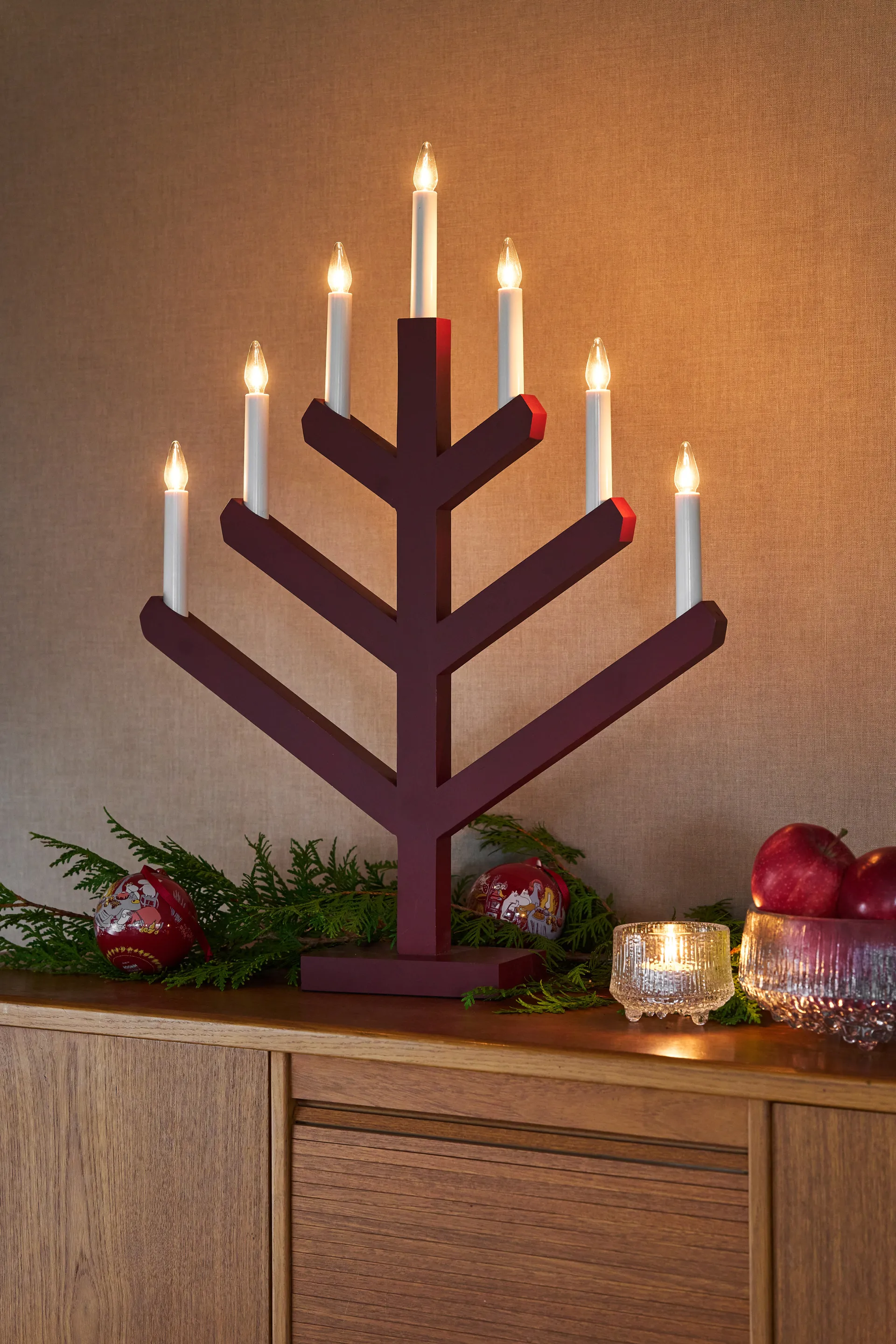Candelabro elettrico in legno bordeaux con sette candele a forma di ramo su una credenza.