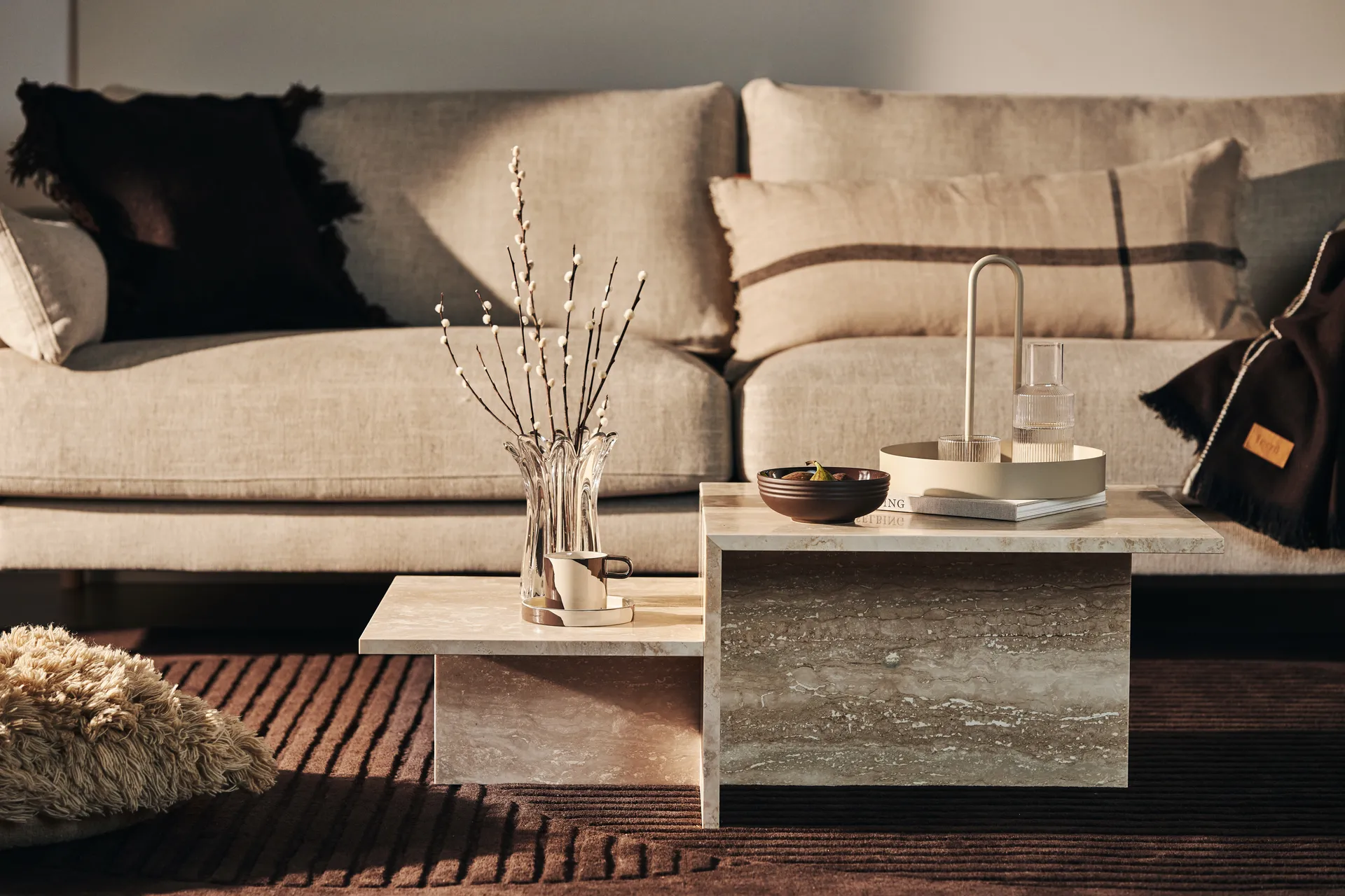 Tavolino a livelli in pietra beige davanti a un divano neutro con accessori decorativi.