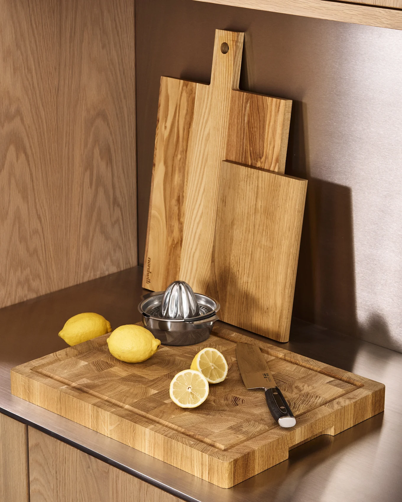 Tre taglieri in legno, uno spremiagrumi in acciaio inossidabile, limoni interi e a metà su un bancone della cucina.