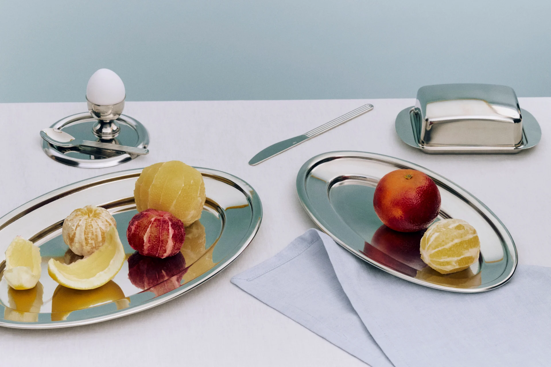 Colazione con agrumi pelati e non pelati su vassoi d'argento, un uovo nel portauovo e una burriera.
