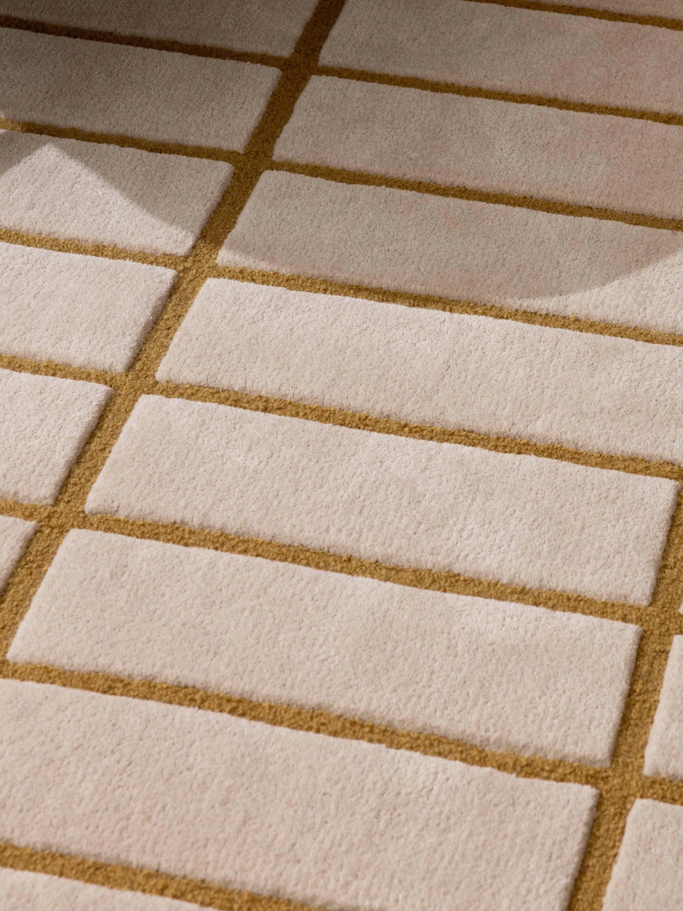 Tappeto a motivi beige e marrone dorato, gamba di poltrona verde e vassoio con teiera e tazza bianche.