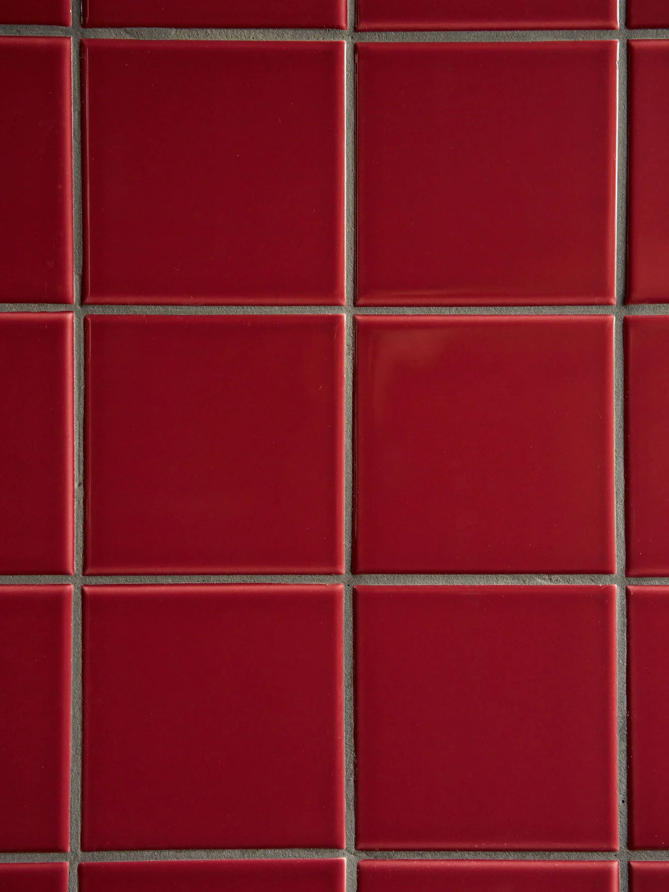 Una griglia di piastrelle rosse quadrate lucide con fughe grigio scuro.