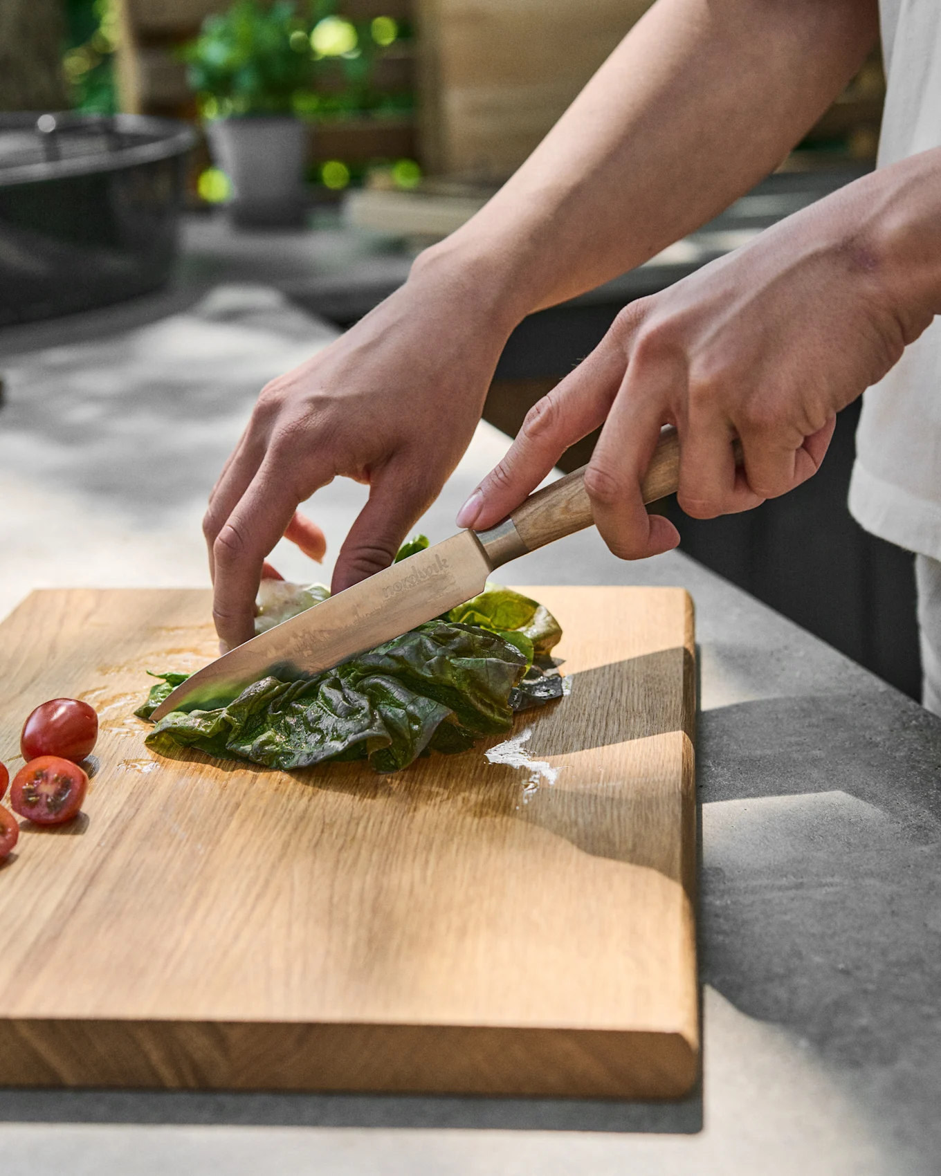 Mani che affettano lattuga verde su un tagliere di legno accanto a pomodorini.