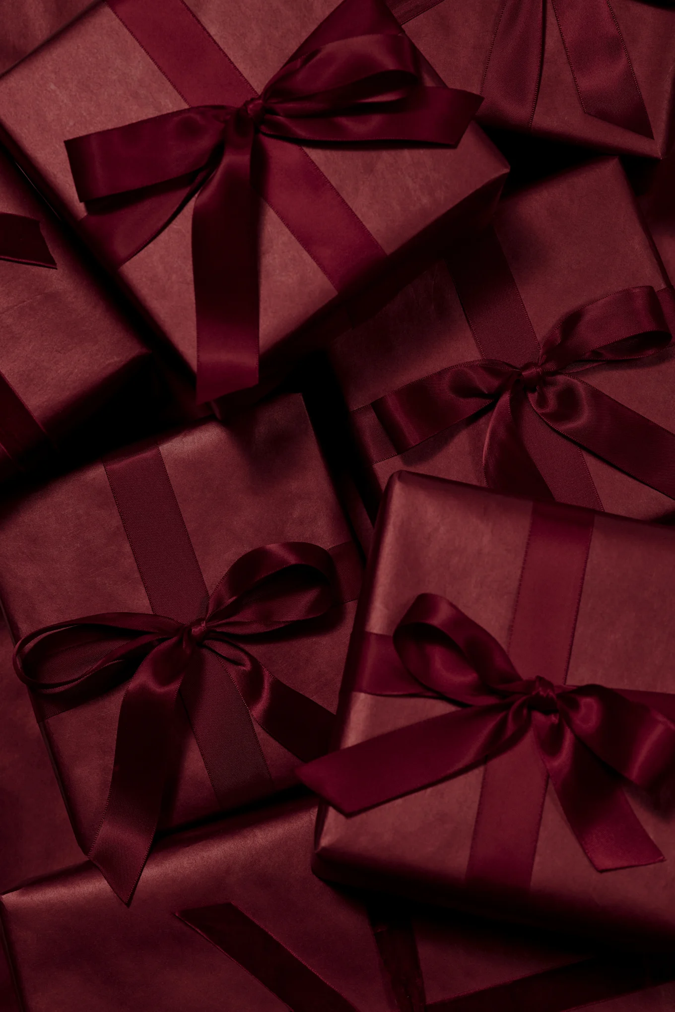 Molteplici scatole regalo rosso scuro avvolte con nastri e fiocchi di raso abbinati.