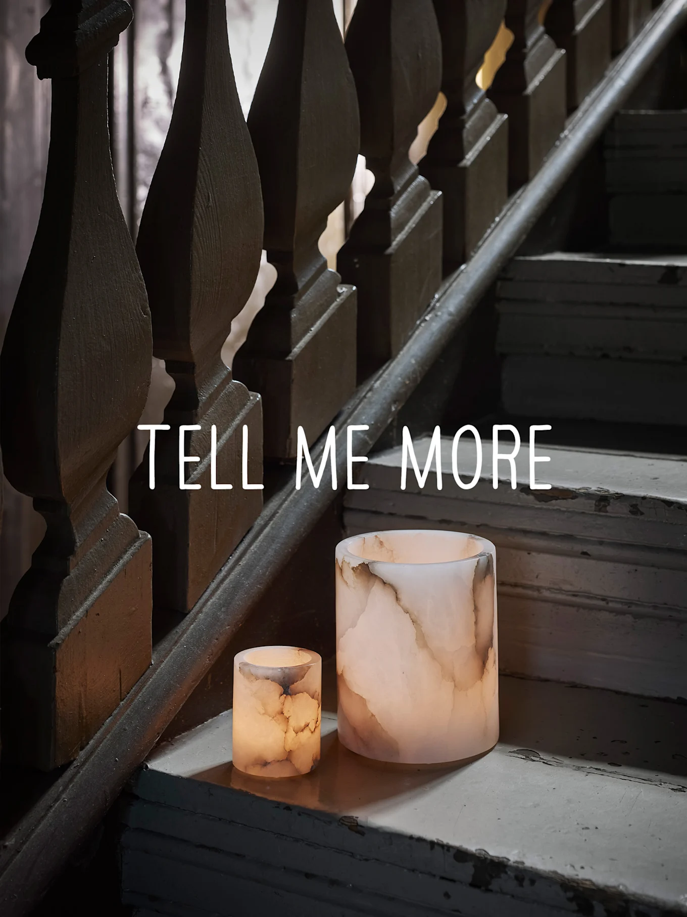 Due portacandele luminosi effetto onice su una scala di legno consumata, con il testo "TELL ME MORE".