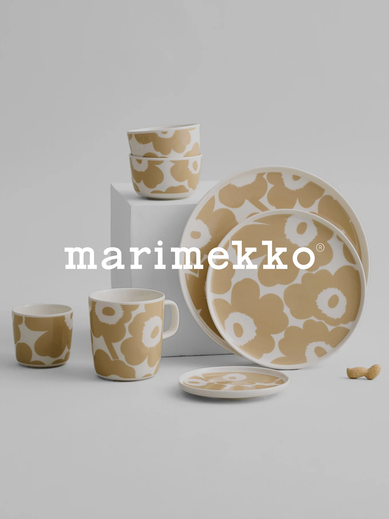 Servizio da tavola Marimekko con motivo floreale beige e bianco, con ciotole, tazza, tazze, piatti e una nocciolina su una superficie grigia.