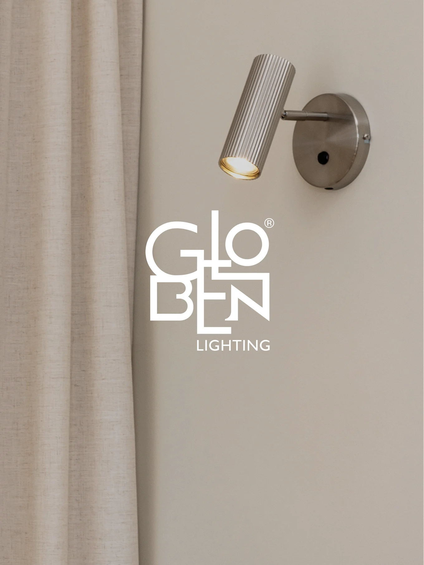 Un faretto da parete in metallo spazzolato e scanalato con un bagliore caldo, accanto a una tenda chiara, con il logo Globen Lighting.