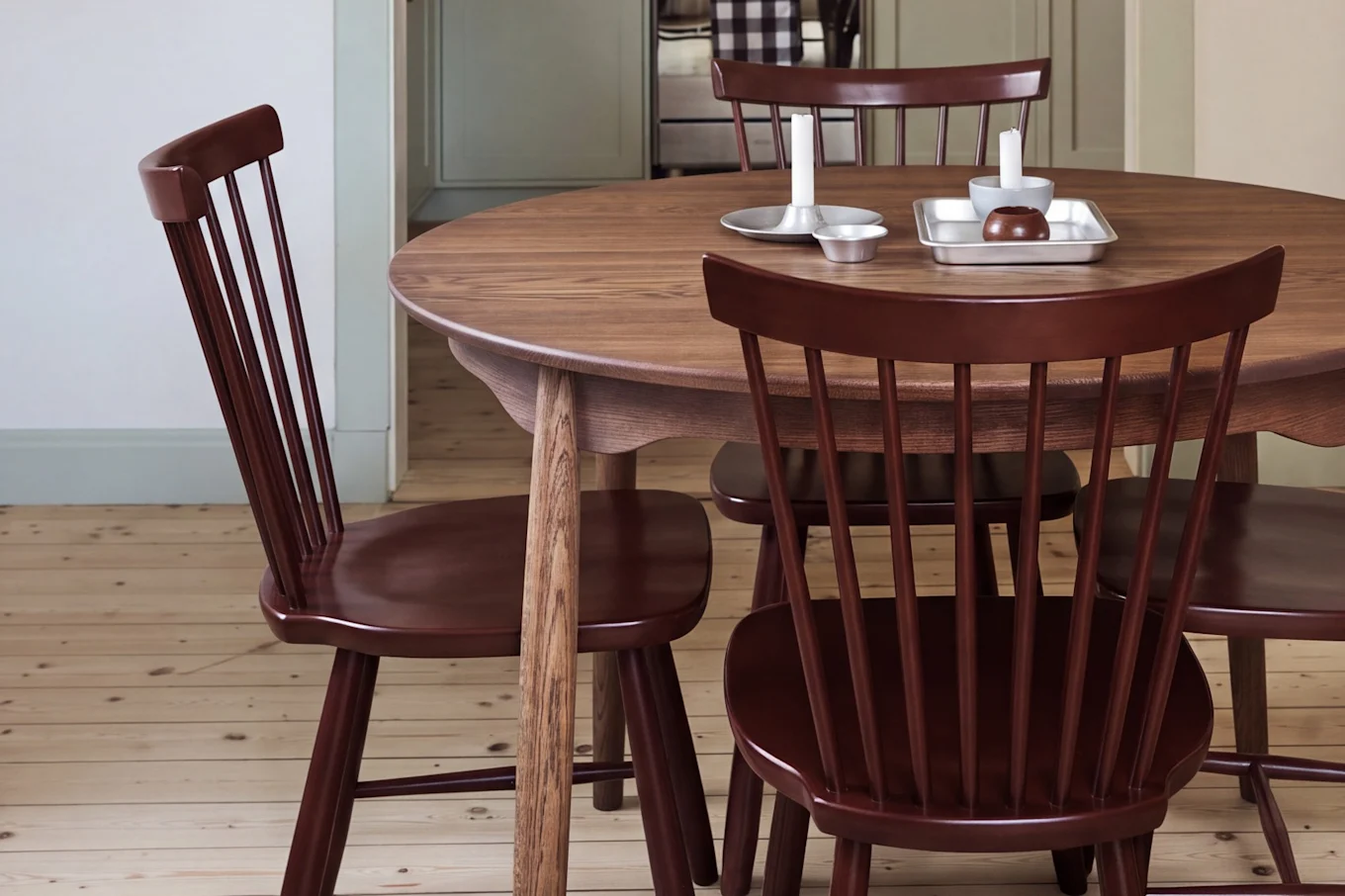 Sala da pranzo con tavolo rotondo in legno, sedie rosse e lampada a sospensione rossa, con vista su una cucina con mobili verde chiaro.