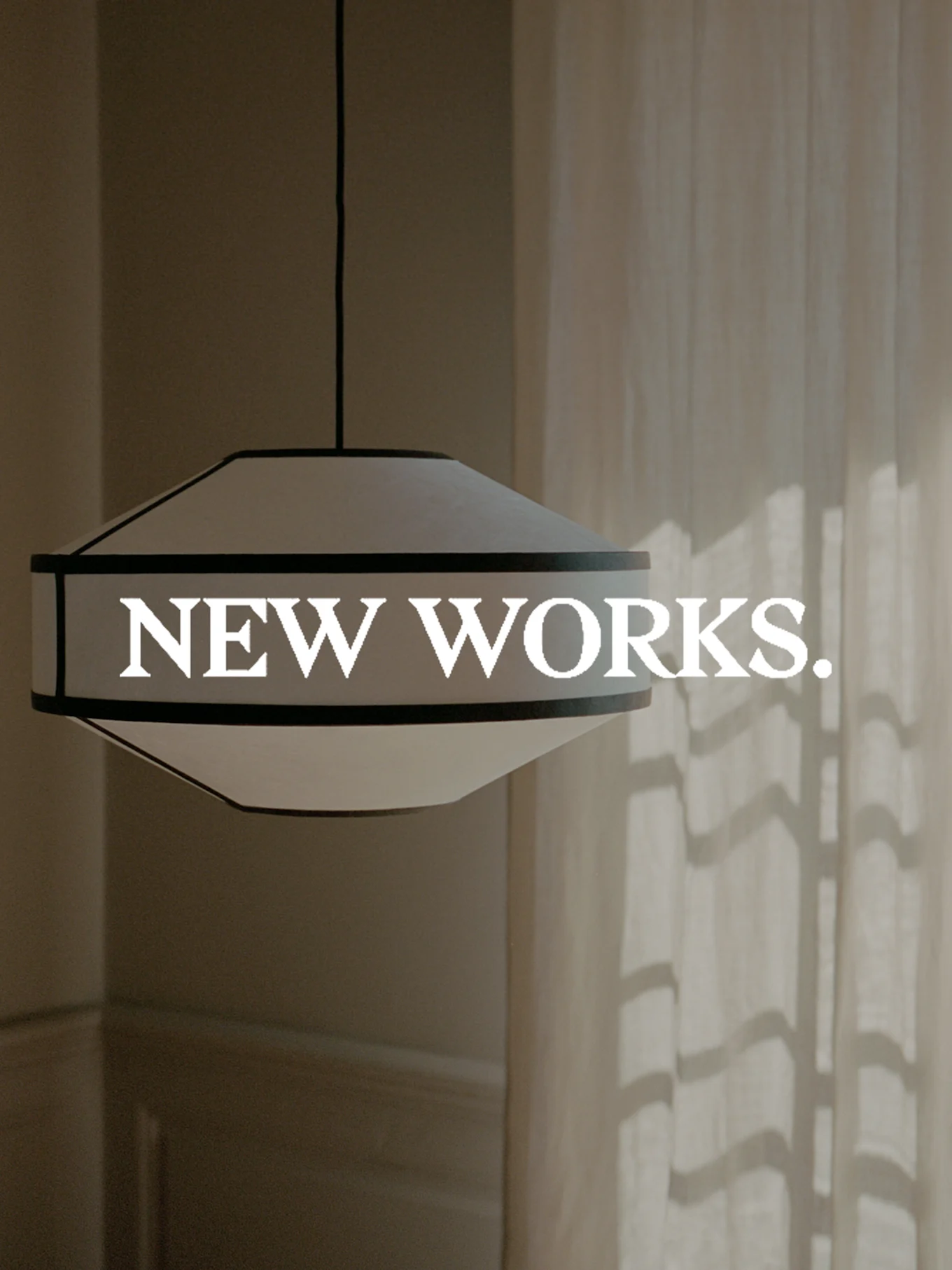 Una lampada a sospensione larga, bianca e con bordo scuro è appesa, con il testo 'NEW WORKS.' sovrapposto. La luce del sole proietta ombre su una tenda.