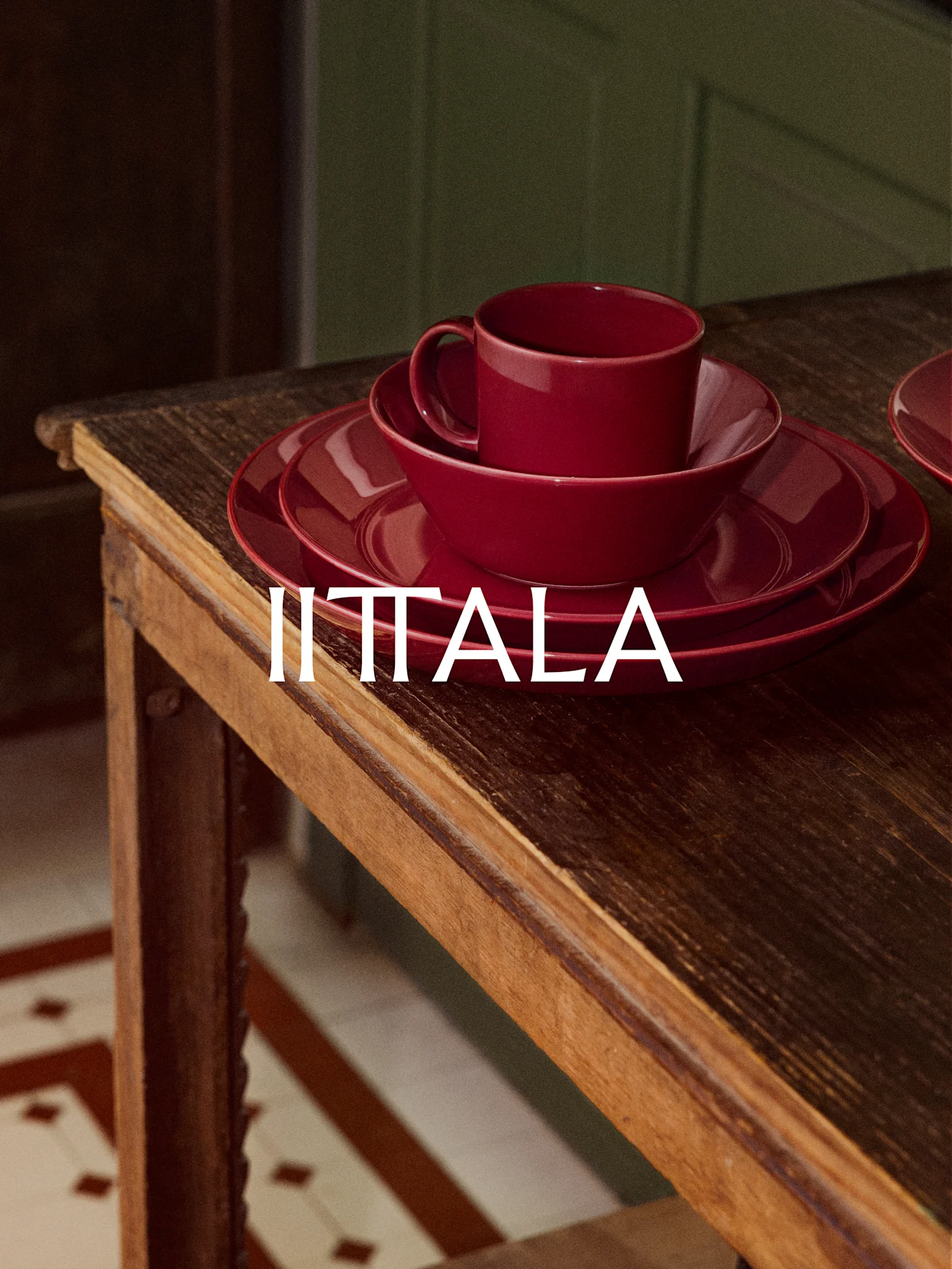 Una pila di stoviglie rosse IITTALA, inclusa una tazza, una ciotola e piatti, si trova su un tavolo di legno rustico.