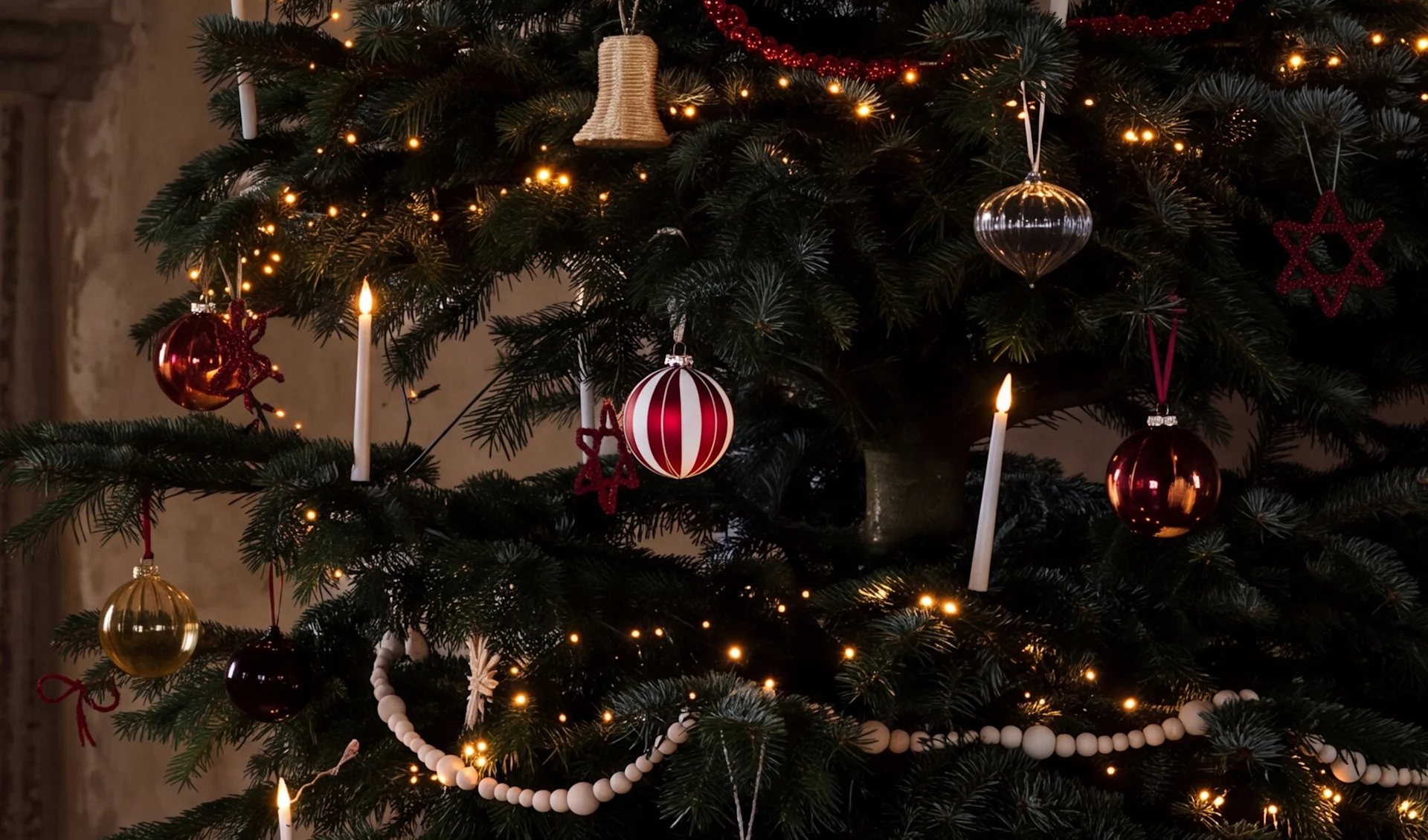Un albero di Natale decorato con luci calde, palline rosse, argentate e dorate, candele bianche e ghirlande di perline di legno.