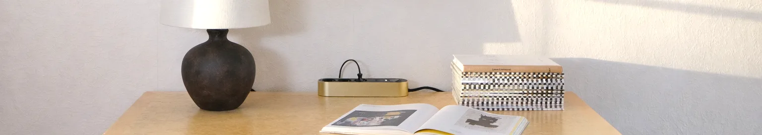 Ciabatta dorata con tre prese nere e un pulsante di accensione su una superficie chiara.