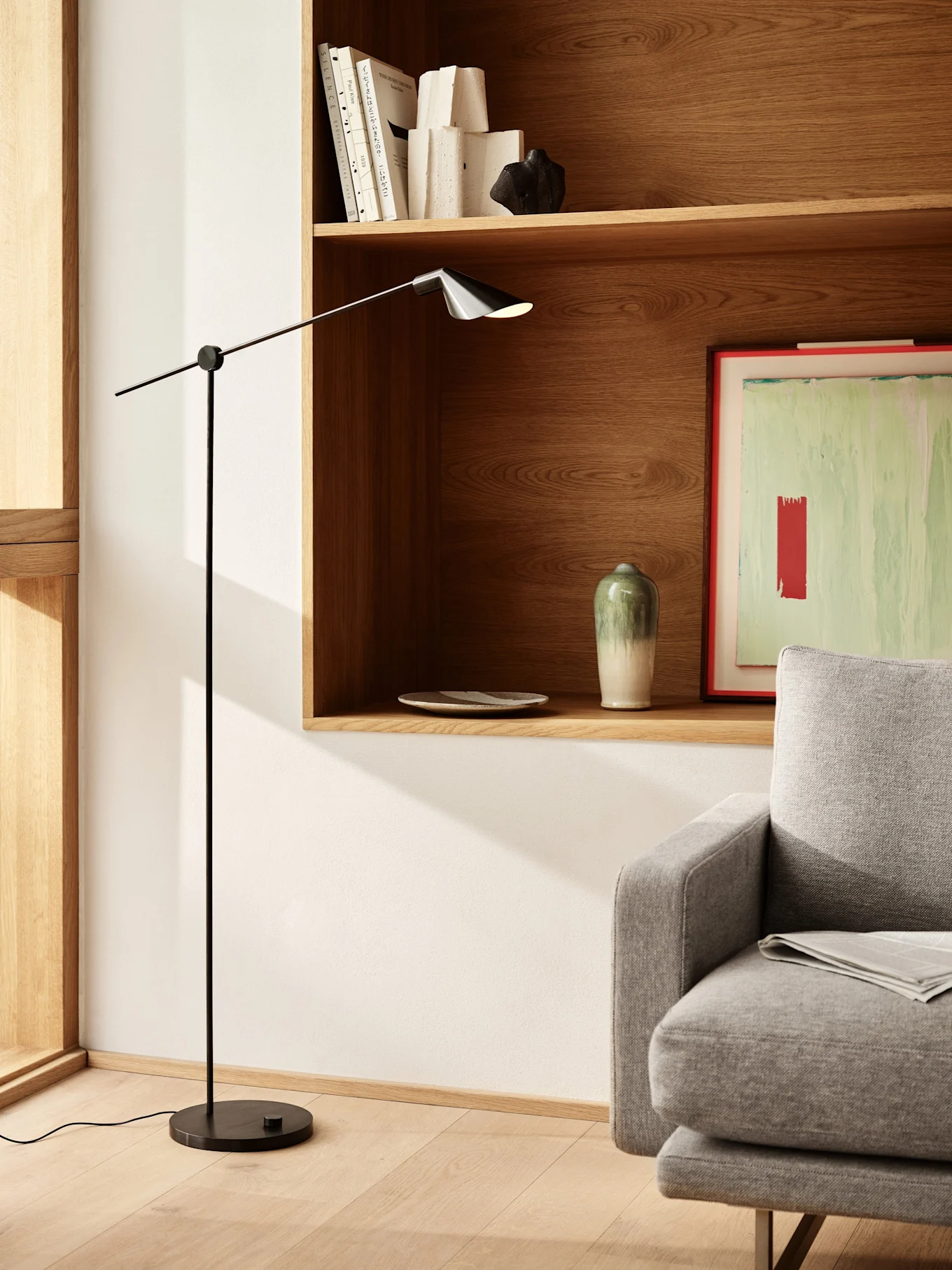 Un soggiorno moderno con una lampada da terra nera elegante, mensole in legno con libri e decorazioni, e parte di un divano grigio.