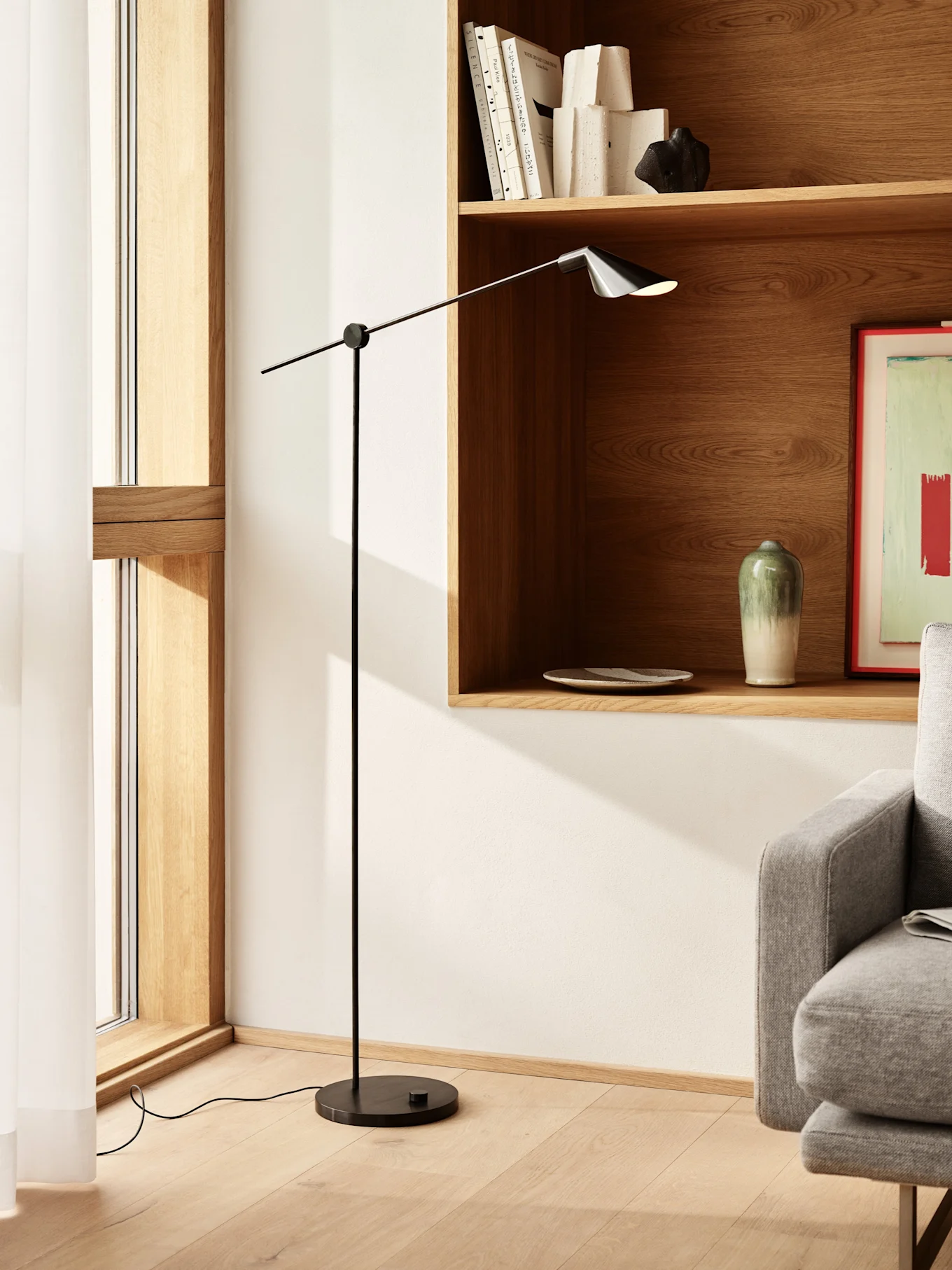 Lampada da terra nera alta e sottile con braccio regolabile e paralume scuro in un soggiorno moderno con mensole in legno.