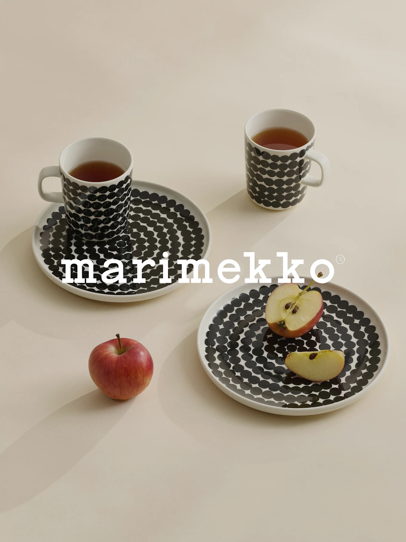 Due tazze e piatti a pois neri, tè, mela rossa, logo Marimekko.