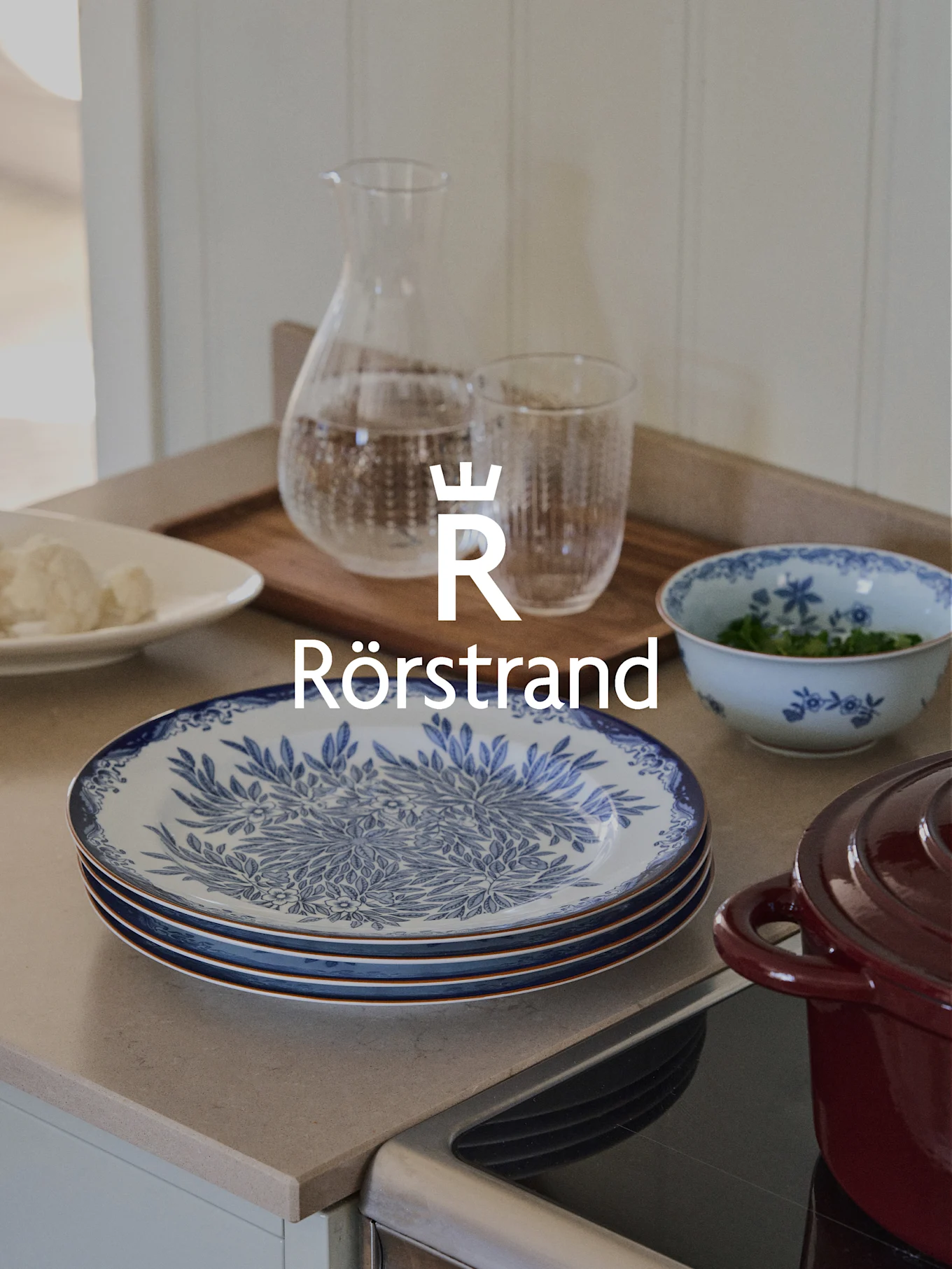 Logo Rörstrand su bancone cucina con piatti blu e bianchi, caraffa, bicchiere e pentola rossa.