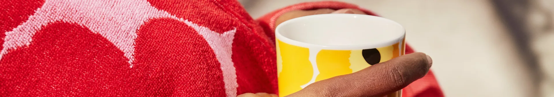 Persona che tiene una tazza gialla con design astratto, avvolta in un asciugamano rosso fantasia.