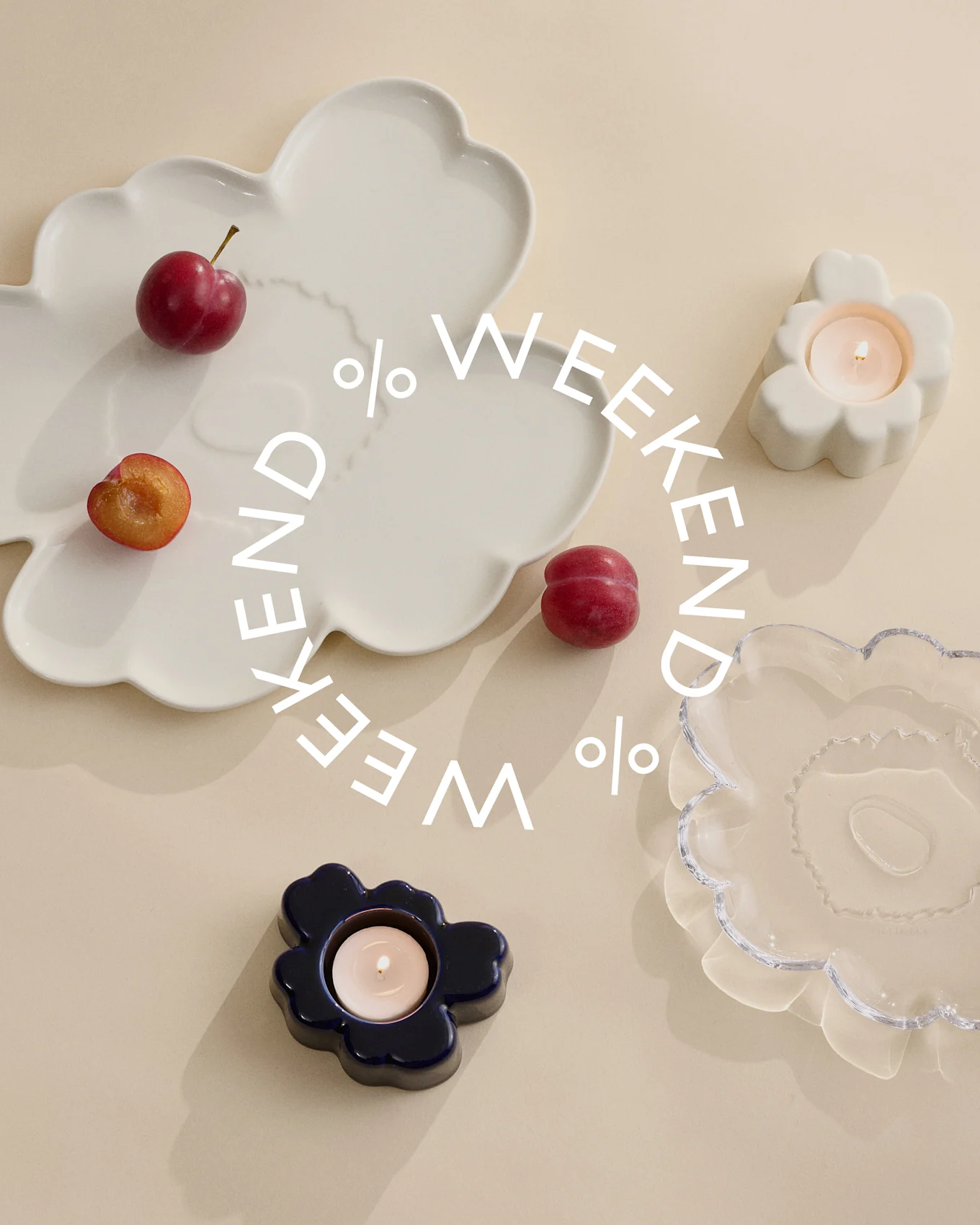 Piatti decorativi e portacandele in vetro bianco, blu e trasparente con prugne su sfondo beige. Testo bianco 'Weekend %'.