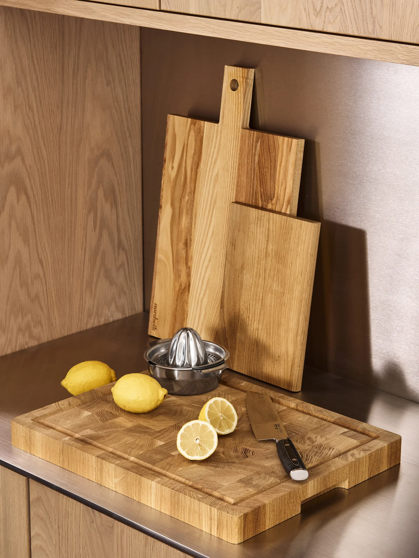Tre taglieri in legno, uno spremiagrumi in acciaio inossidabile e limoni freschi su un bancone da cucina.