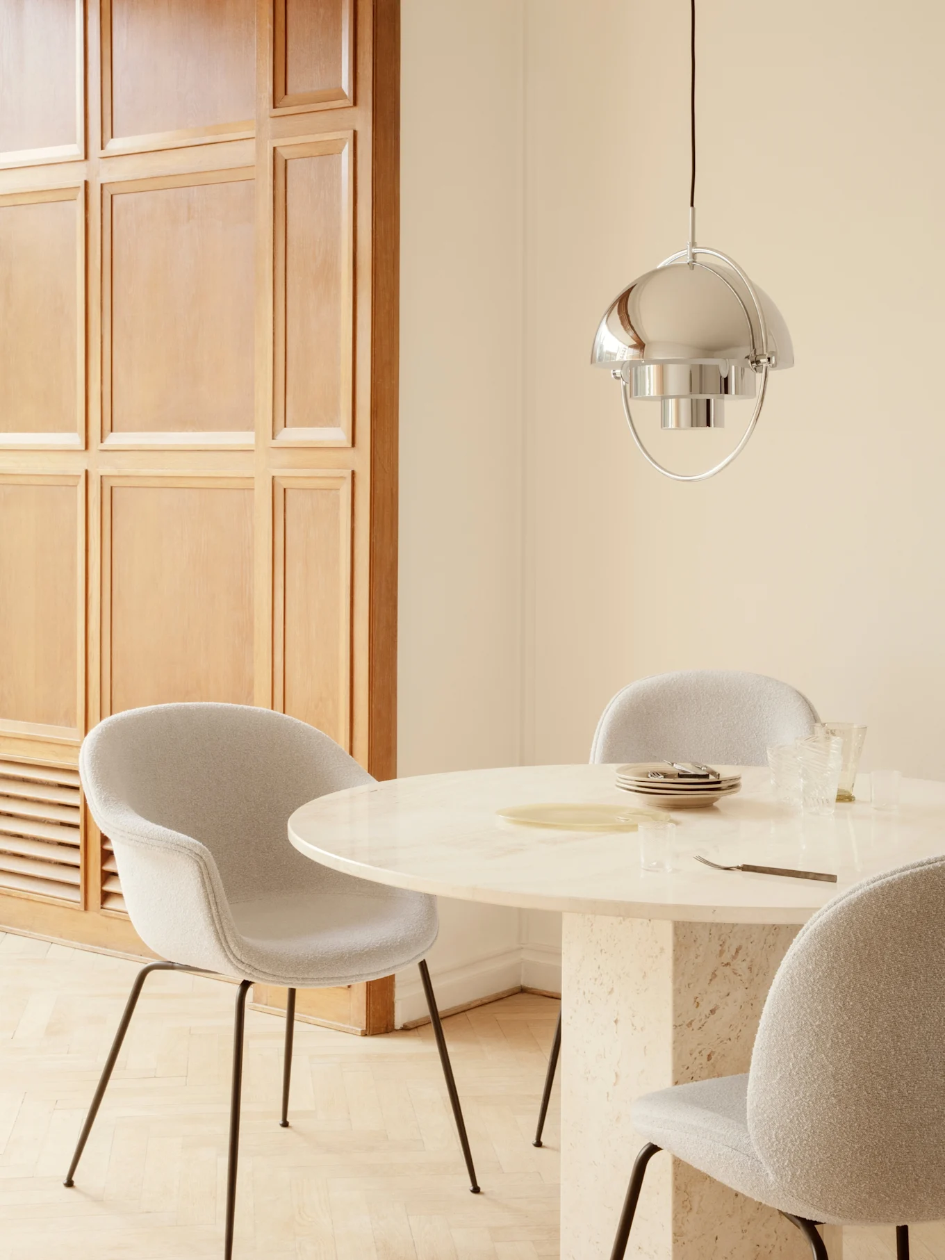 Sala da pranzo con tavolo rotondo in marmo, sedie imbottite grigio chiaro e lampada a sospensione in argento lucido.