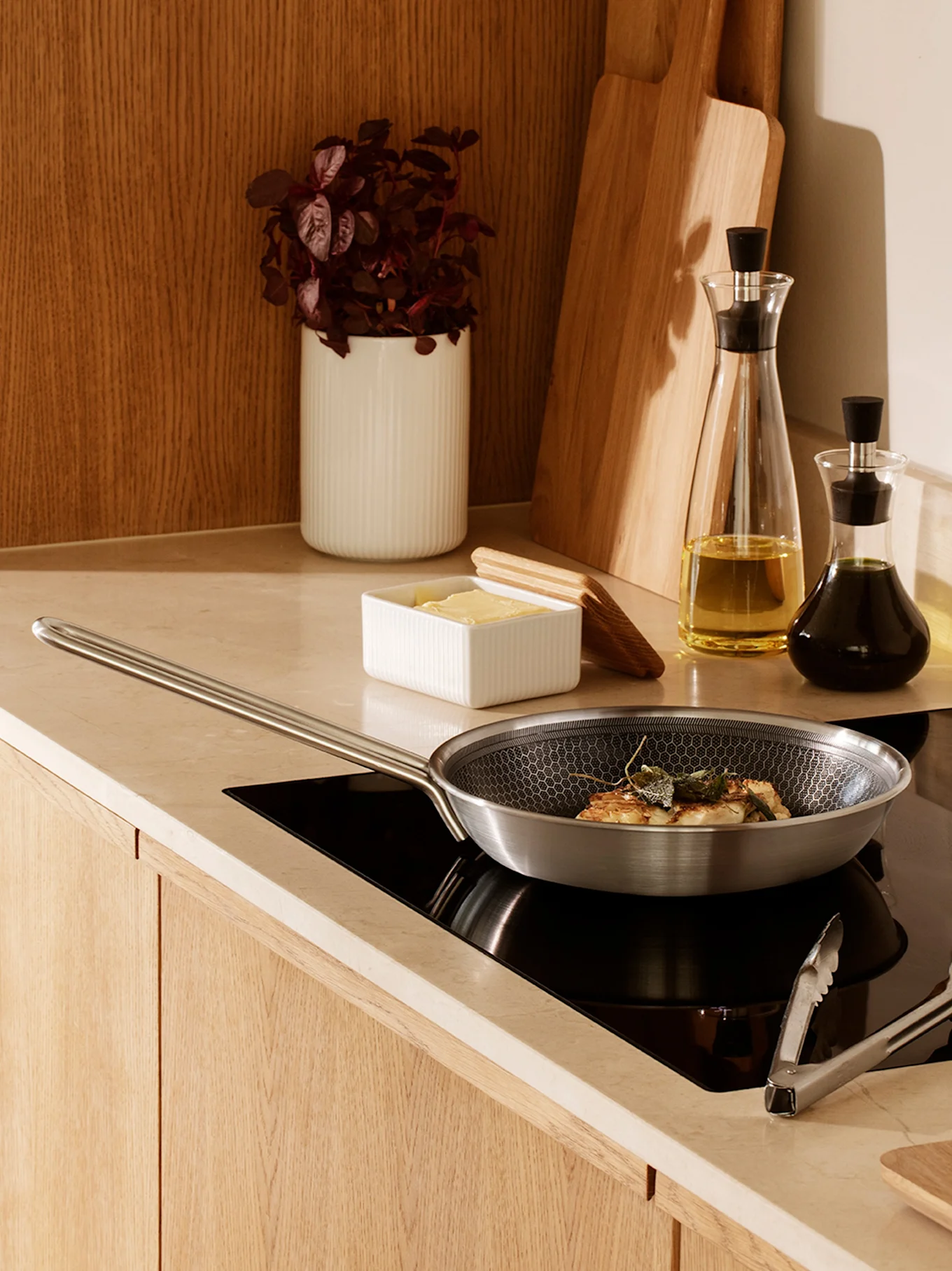 Una padella in acciaio inossidabile con motivo a nido d'ape cucina cibo con salvia su un piano cottura a induzione nero in una cucina moderna.