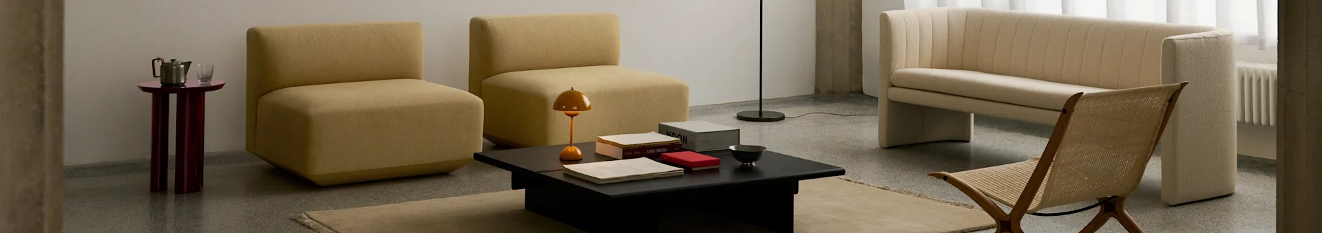 Un soggiorno moderno con due poltrone color senape senza braccioli, un tavolino nero, un divano a coste crema e una sedia in legno intrecciato.