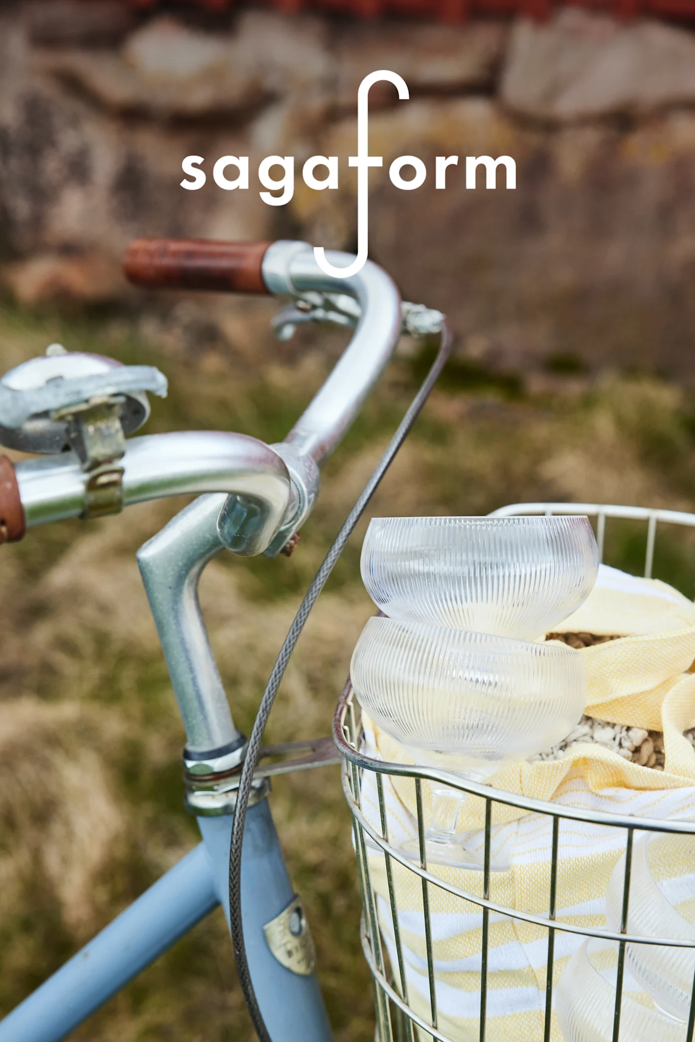 Due ciotole in vetro trasparente a coste e un asciugamano a righe gialle in un cestino da bicicletta. Logo 'sagaform'.
