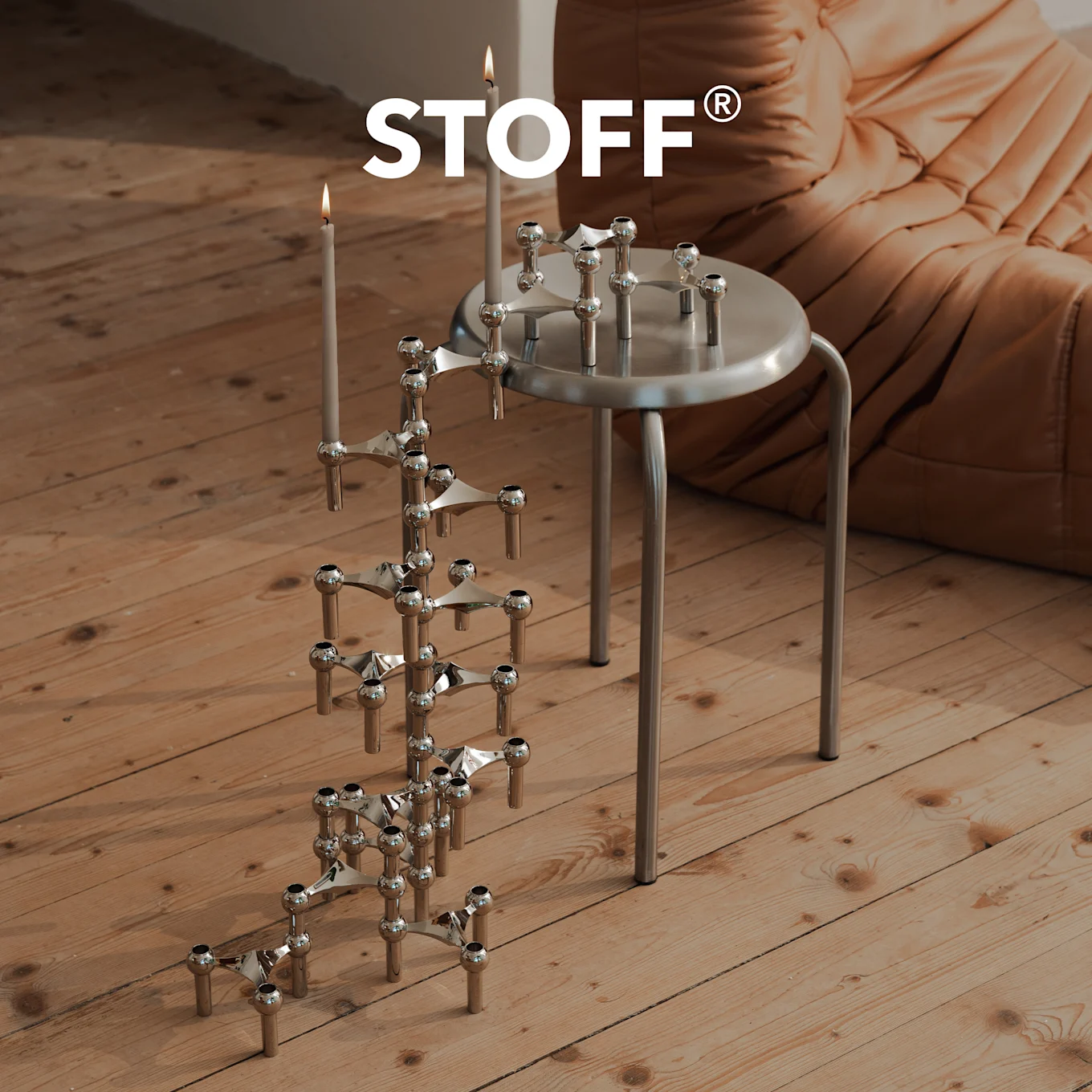 Logo STOFF sopra candelabro cromato con candele su pavimento in legno, e un altro su uno sgabello argentato.