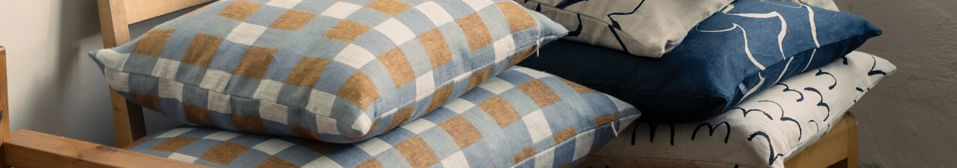 Cuscini impilati su una sedia di legno, con motivi a quadri blu e marroni e disegni astratti blu e beige.