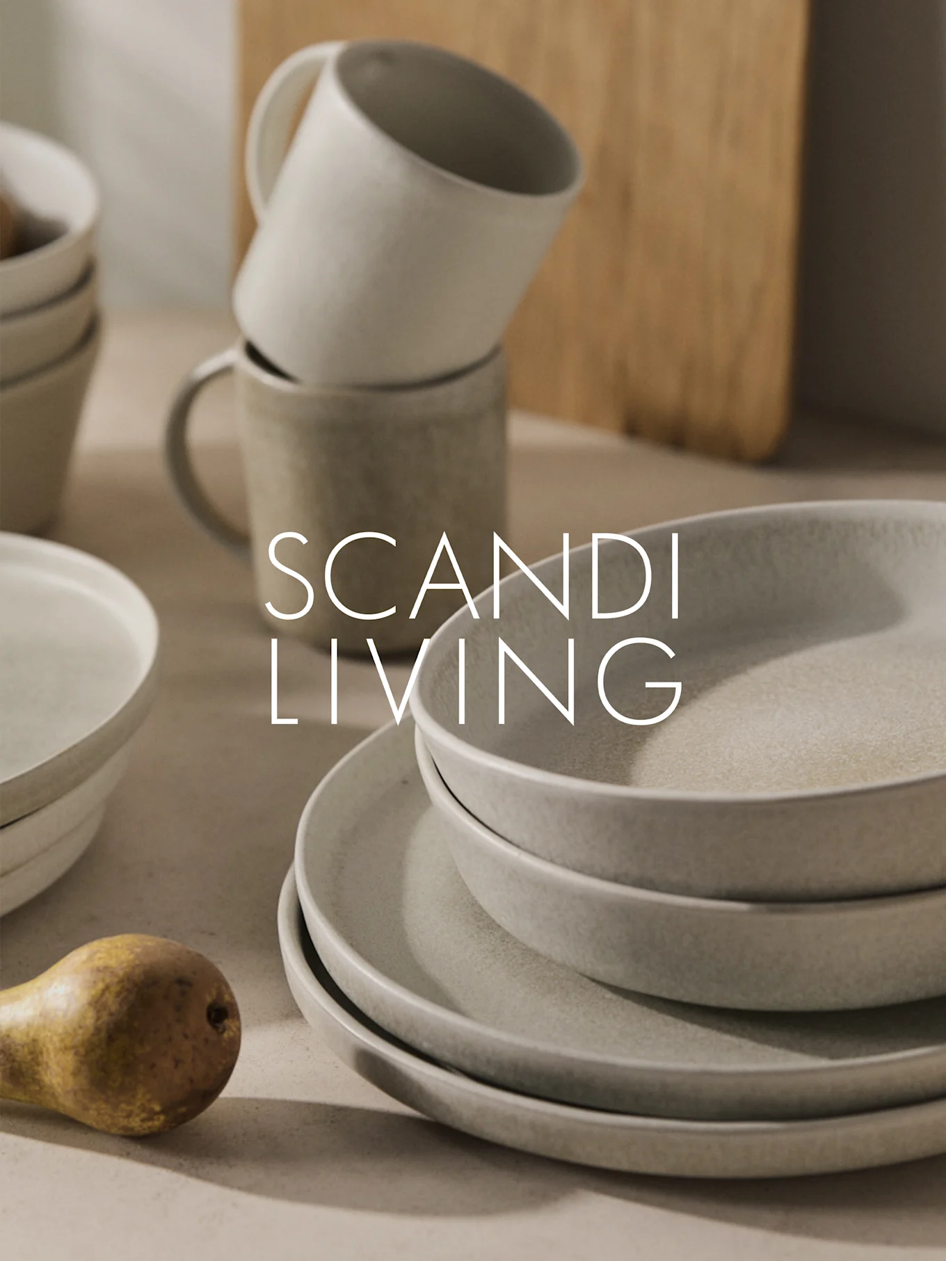 Stoviglie in ceramica beige impilate, tazze e una pera con scritta "SCANDI LIVING".