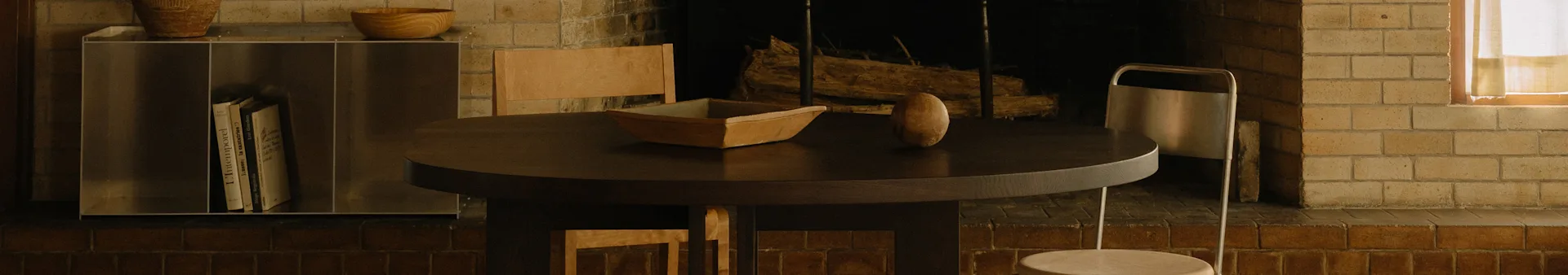 Una zona pranzo accogliente con un tavolo rotondo in legno scuro, una ciotola di legno, un oggetto ovale, sedie e un camino.