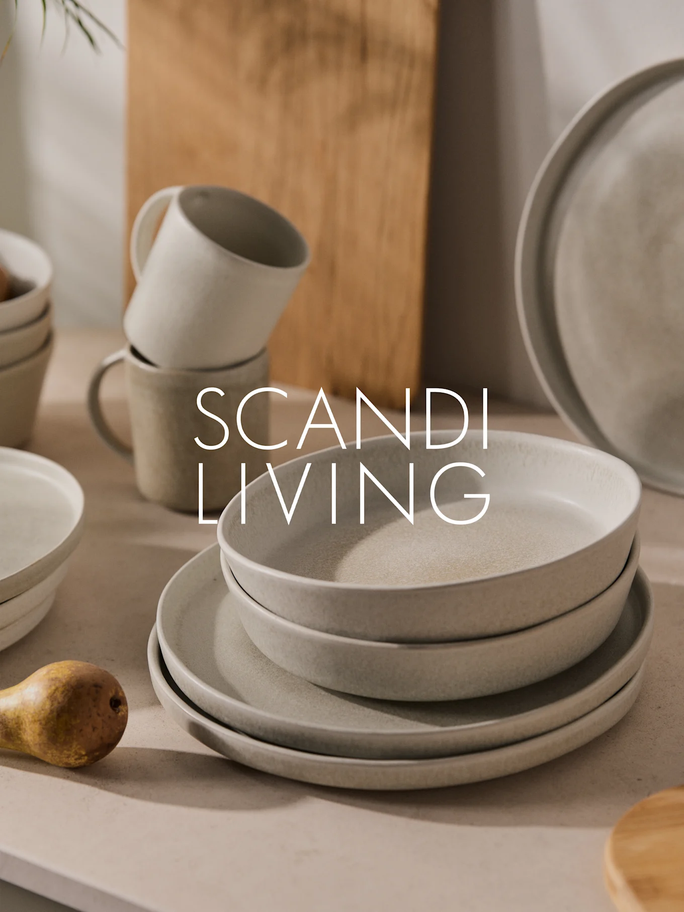 Pila di piatti, ciotole e tazze in ceramica chiara maculata con una pera. Testo: SCANDI LIVING.