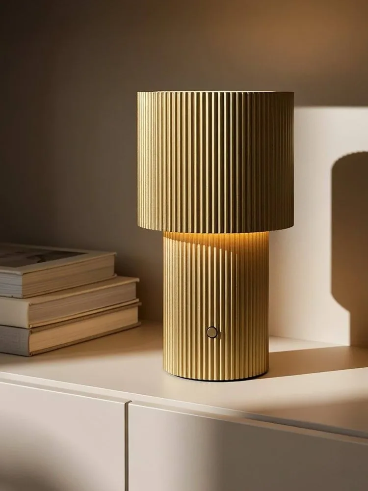 Lampada da tavolo dorata a coste, luminosa, con un pulsante circolare sulla base.