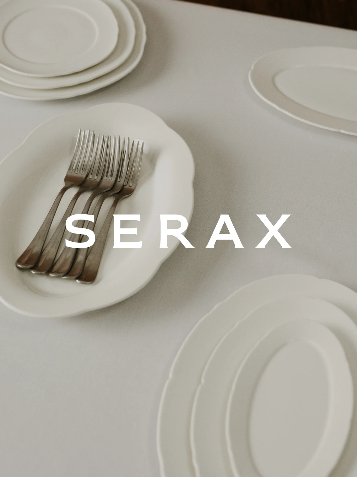 Tavola apparecchiata con piatti e forchette bianche, con testo 'SERAX' sovrapposto.