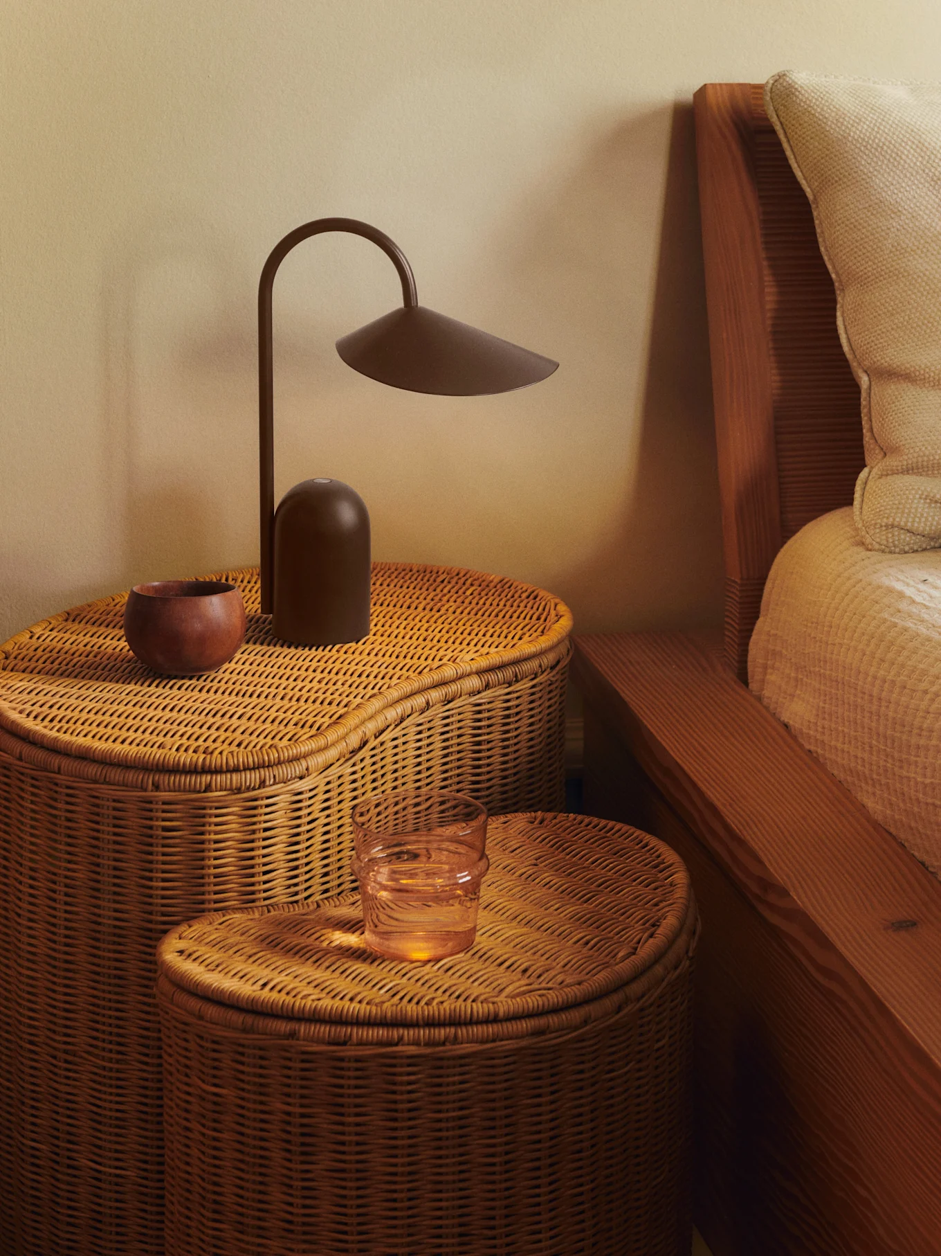 Due comodini in rattan intrecciato con lampada marrone scuro, ciotola in legno e bicchiere d'acqua.