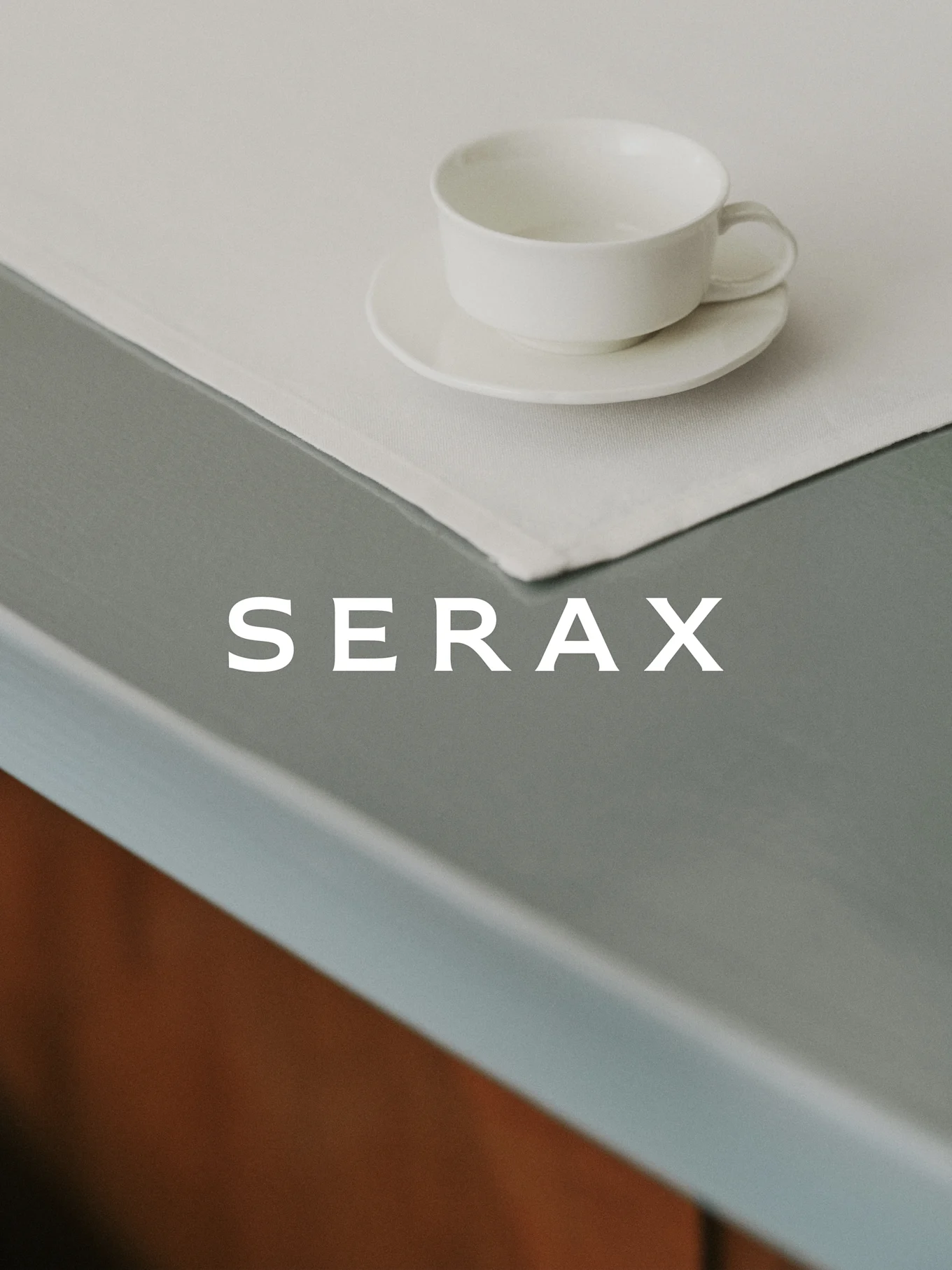 Una tazza da tè bianca e piattino su una tovaglietta di lino chiaro su un tavolo grigio con la parola SERAX.