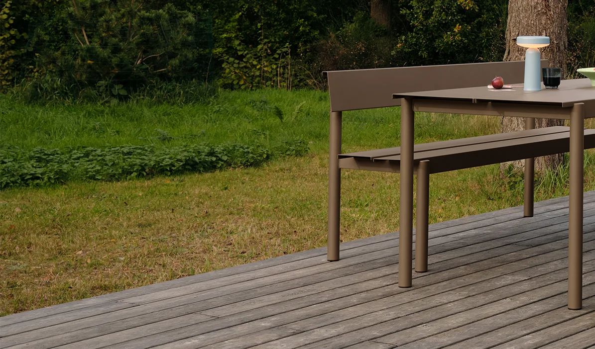 Tavolo e panca da pranzo moderni color tortora su una pedana in legno, con lampada portatile e mele sul tavolo.