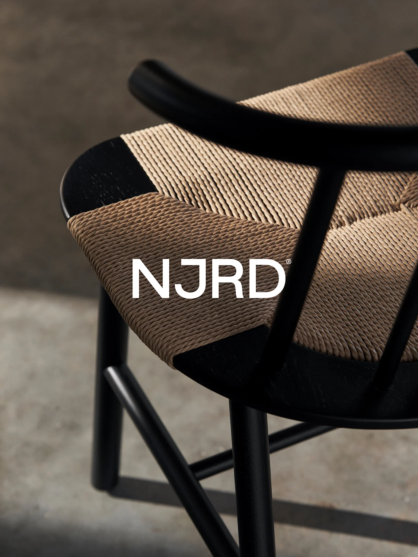 Primo piano di una sedia nera con seduta intrecciata marrone chiaro, con il logo bianco 'NJRD'.