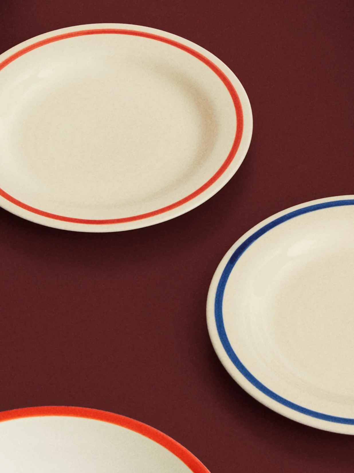 Tre piatti ovali color crema con bordi rossi e blu su una superficie rosso scuro.