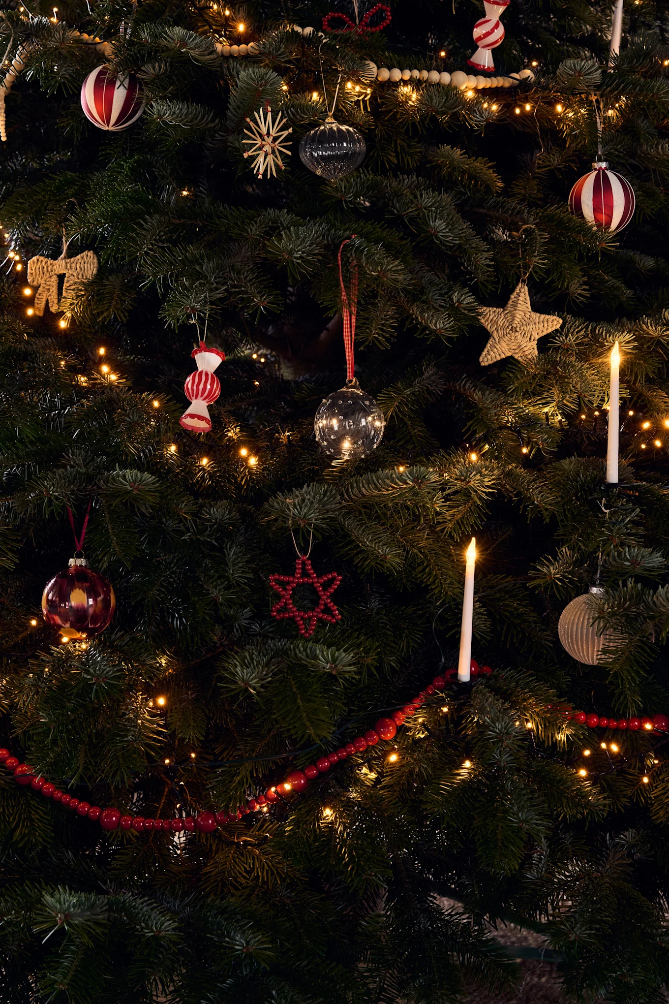 Un albero di Natale riccamente decorato con vari ornamenti, luci calde e candele accese.