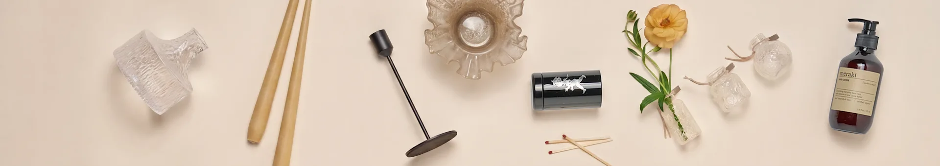 Una collezione di articoli per la casa, tra cui vasi di vetro, bacchette, un candeliere nero, una ciotola di vetro con balze, un contenitore nero, un fiore arancione e una bottiglia di lozione per le mani.