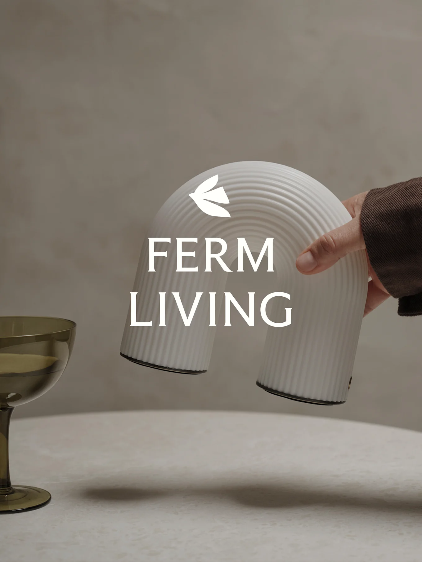 Mano che tiene un oggetto decorativo bianco a coste a forma di arco, con un bicchiere verde vicino.