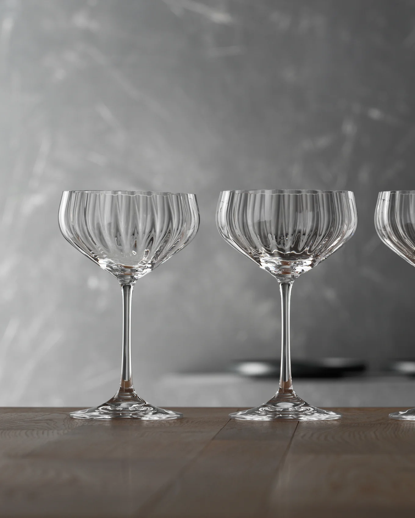 Tre coppe di champagne vuote, trasparenti e a coste su un tavolo di legno con sfondo grigio.