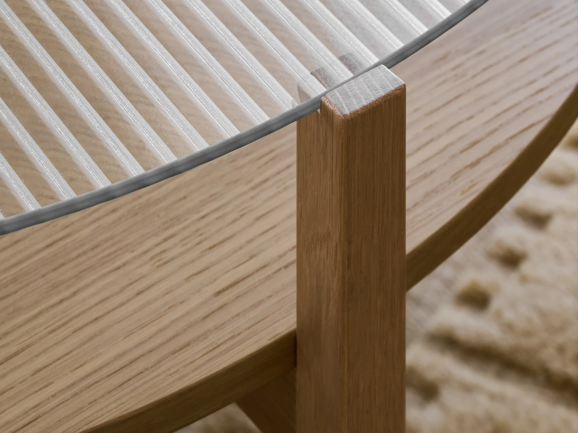 Primo piano di un tavolo con piano in vetro scanalato e gamba in legno marrone chiaro.