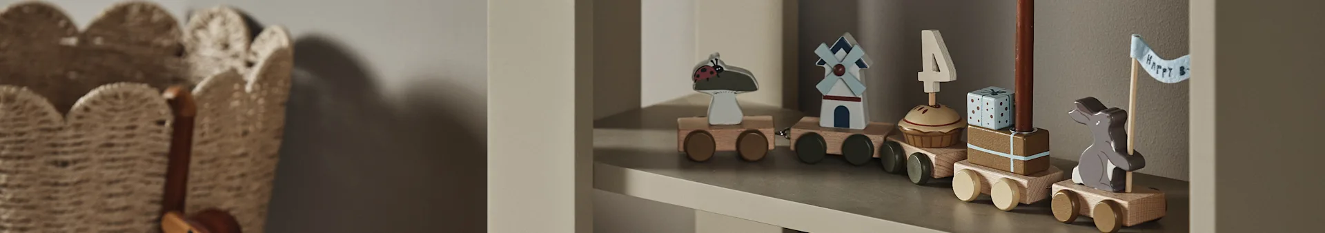 Un trenino di legno su uno scaffale, con vagoni raffiguranti una coccinella, mulino a vento, cupcake con candela '4', un regalo e un coniglietto con bandiera "Happy B".