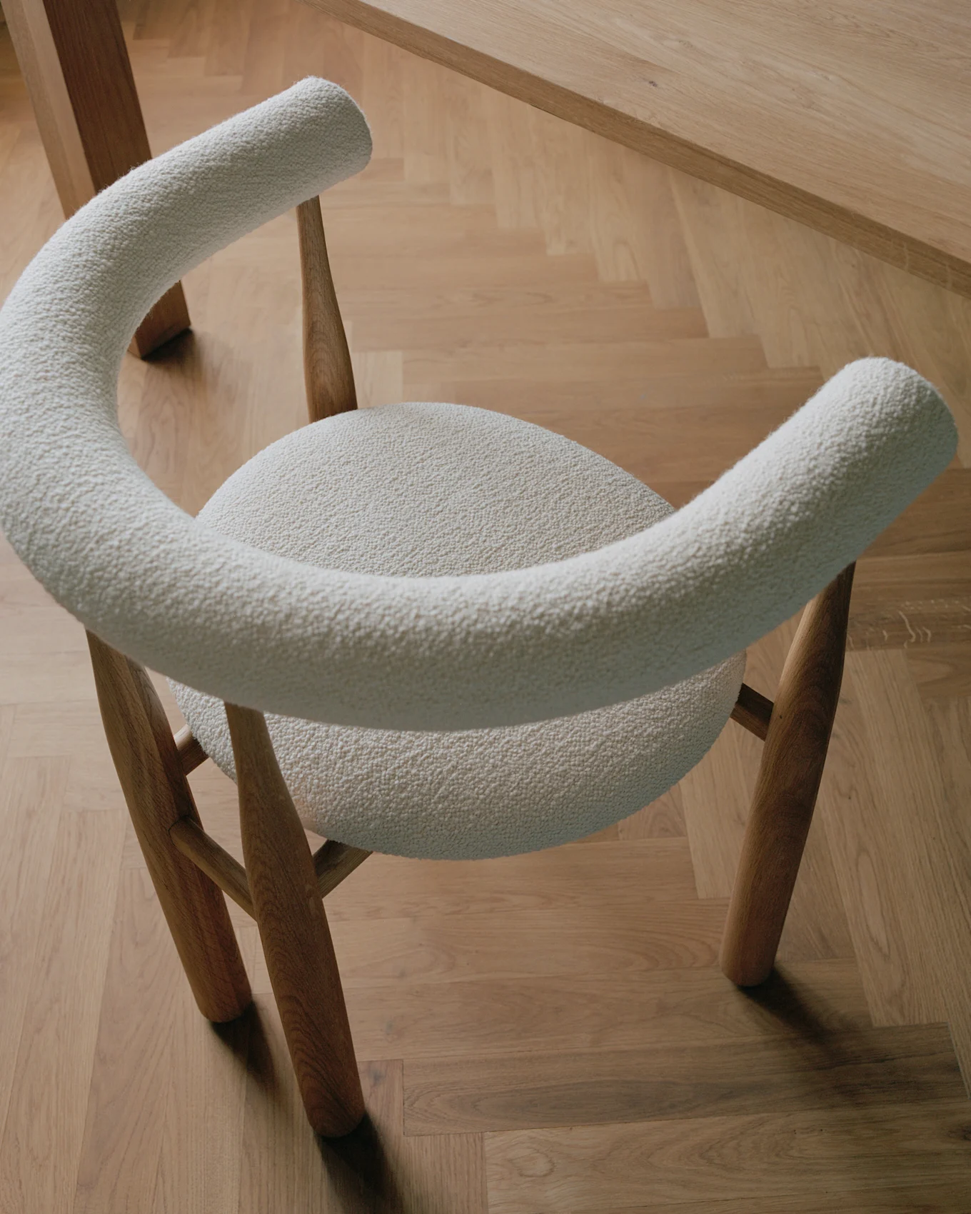 Sedia moderna con rivestimento in bouclé crema chiaro e gambe in legno, su un pavimento in parquet di legno chiaro.