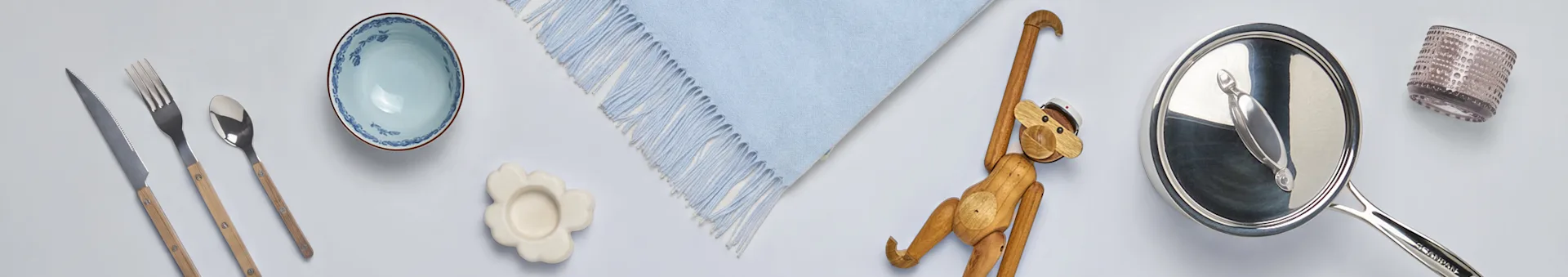 Assortimento di articoli per la casa: posate con manici in legno, ciotola blu, sottobicchiere a fiore, coperta blu, scimmia di legno, pentola e bicchiere.