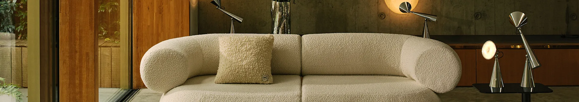 Soggiorno moderno con divano modulare bouclé bianco sporco, un tappeto chiaro fantasia e lampade in metallo.