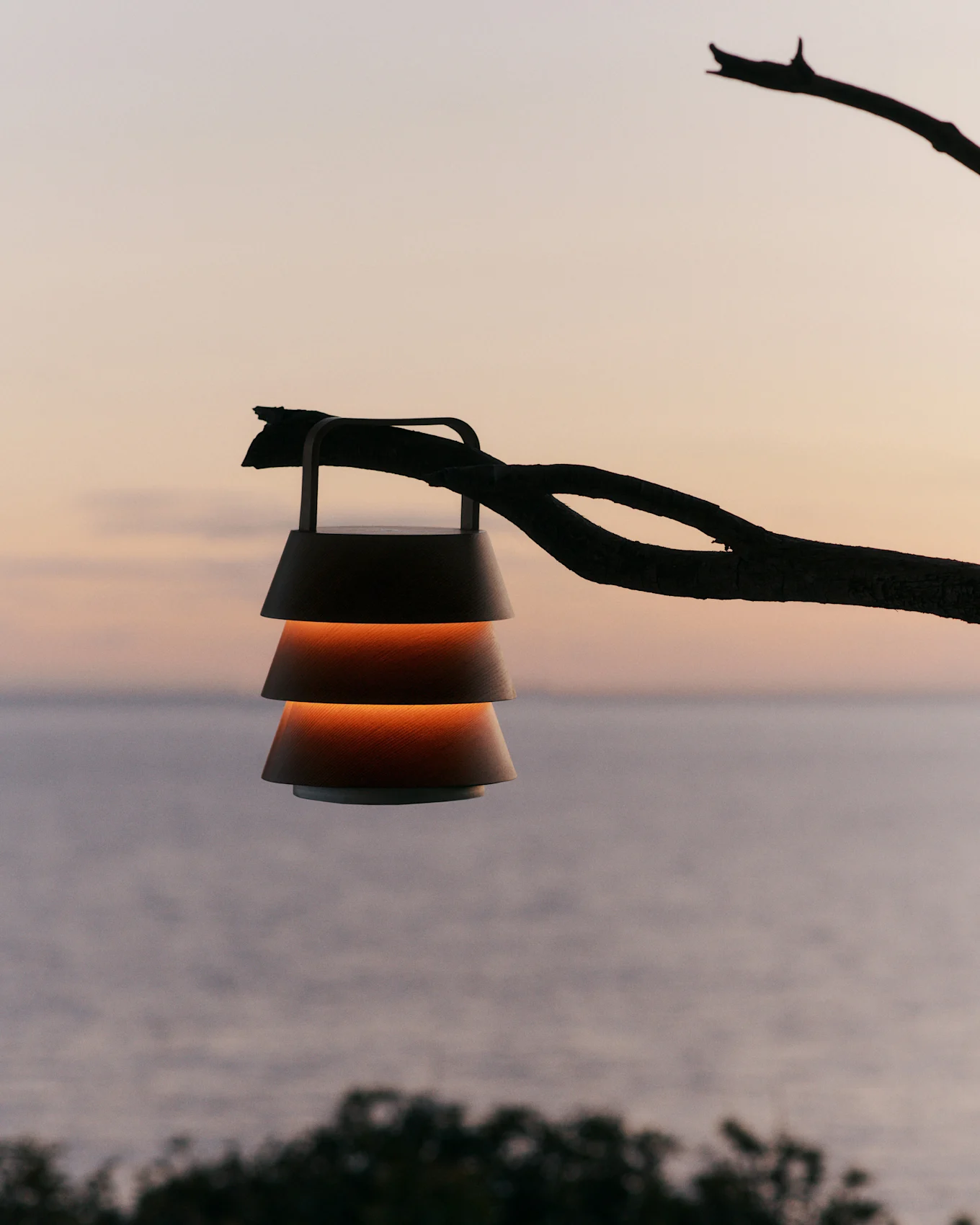 Lanterna con paralumi a strati appesa a un ramo contro un cielo al tramonto sull'acqua.