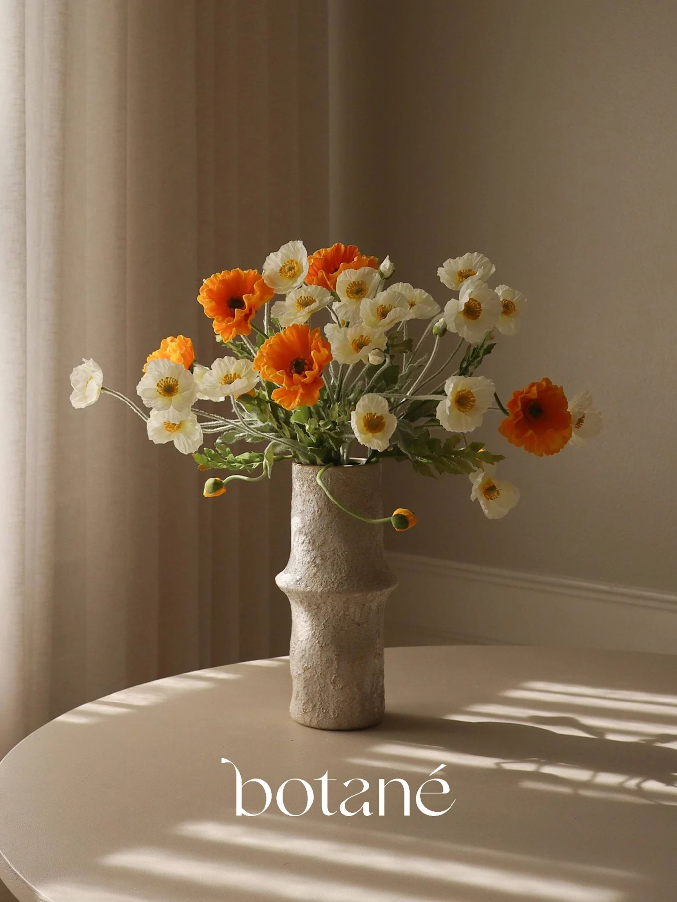 Un vaso testurizzato contiene un bouquet di papaveri finti arancioni e bianchi su un tavolo con ombre a strisce.